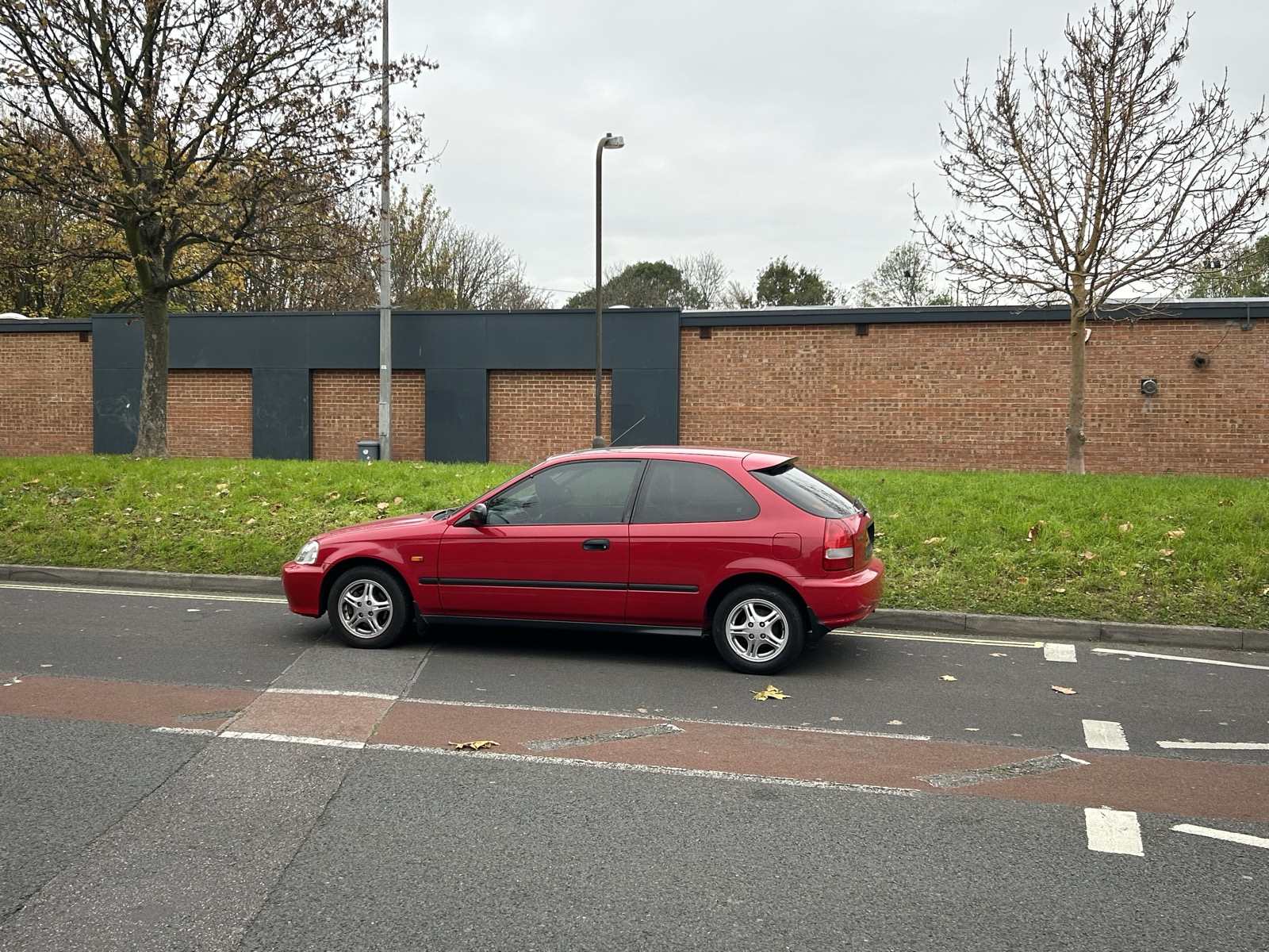 A stock red Honda Civic EK hatchback parked on a residential street, shortly after purchase