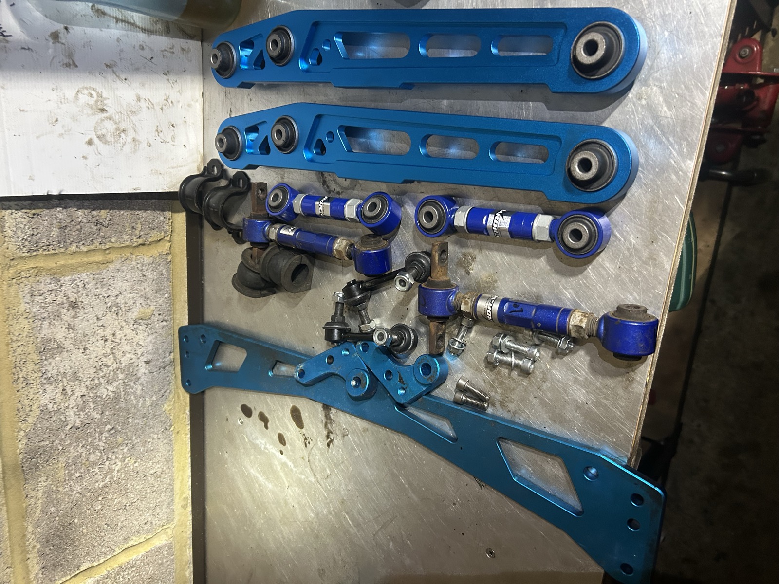 A set of blue Hardrace suspension arms and polyurethane bushes laid out on a workbench