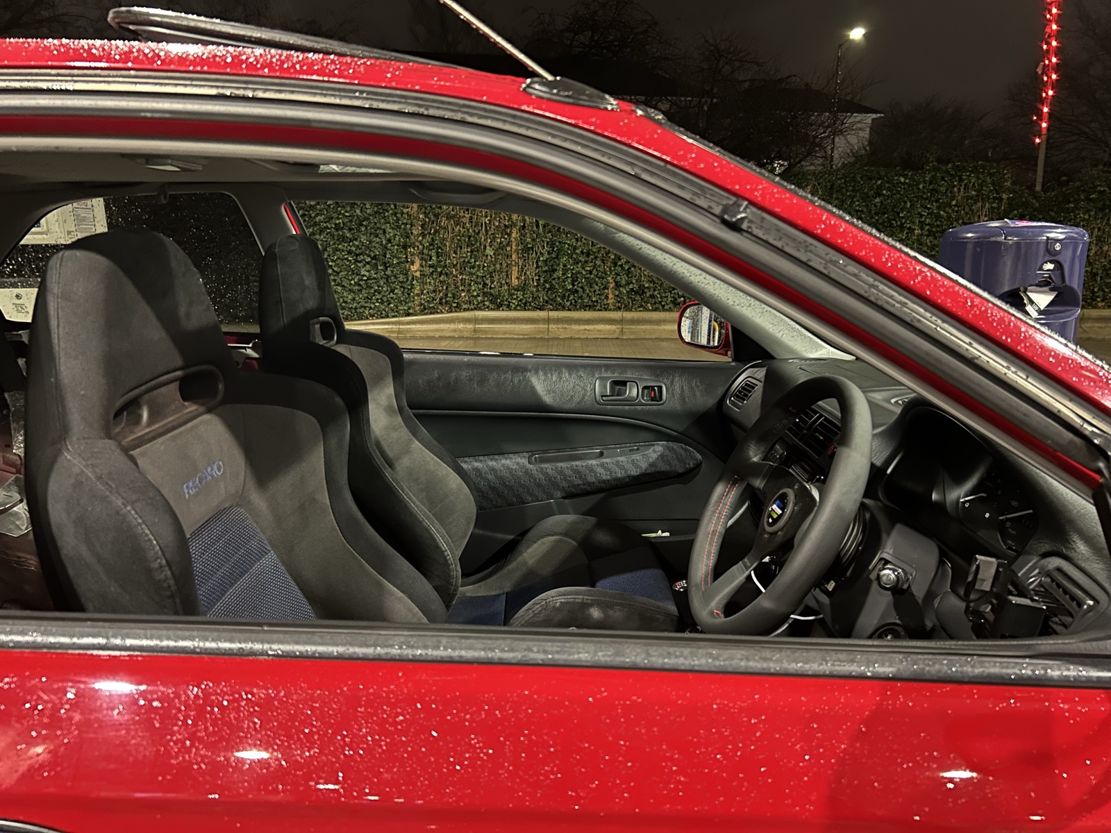 Night-time view into the Civic EK through the open door, showing the bucket seats and Spoon steering wheel
