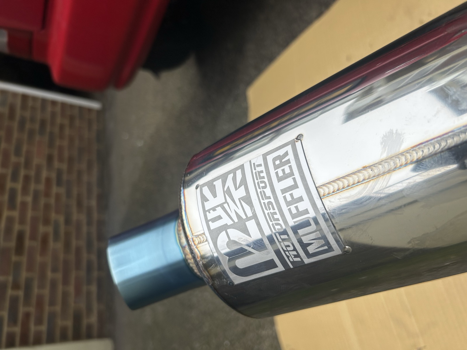 A polished M2 Motorsport muffler, branded, sitting on a workbench