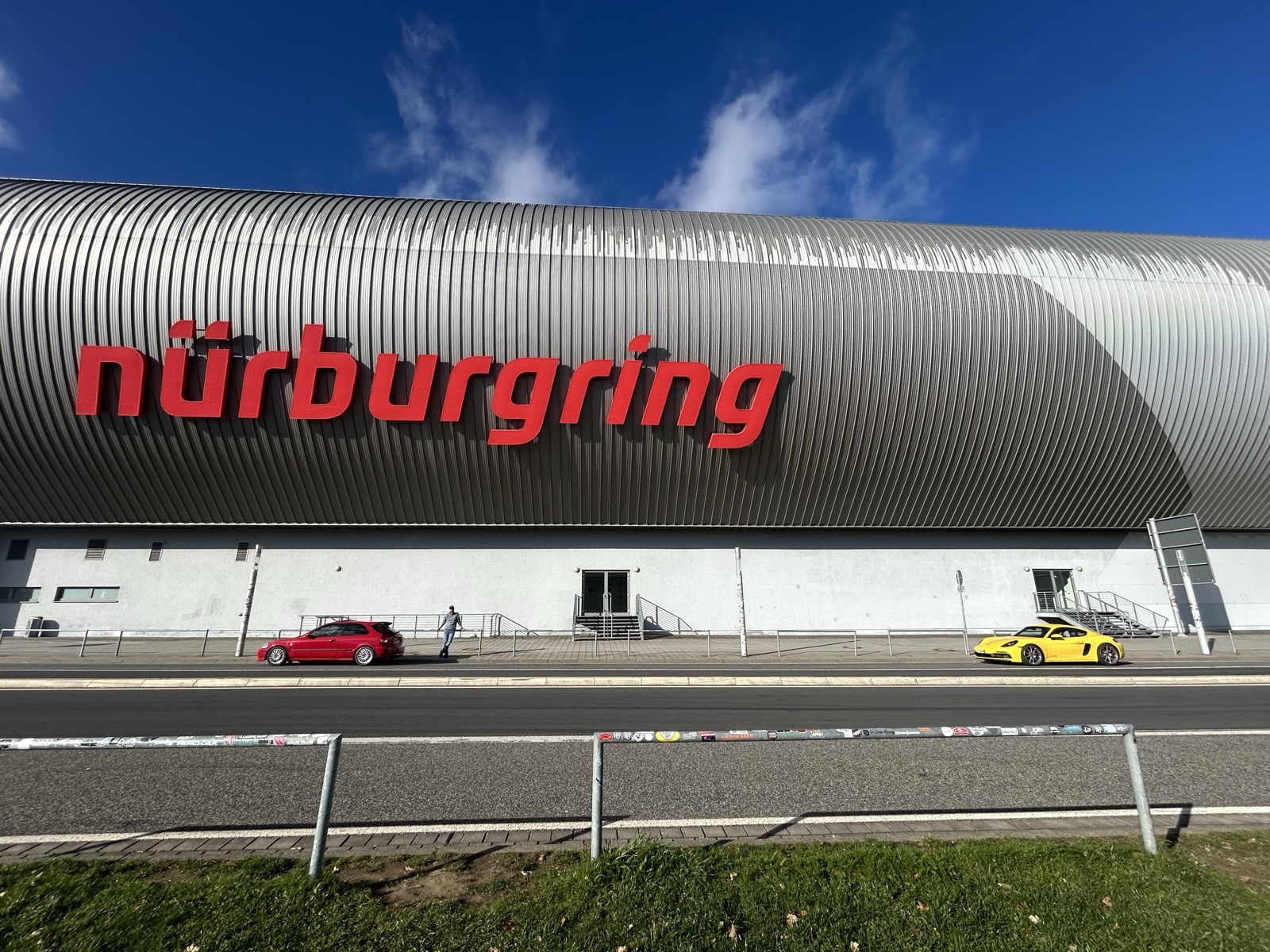 The red Civic EK parked near the Nurburgring sign, with a yellow Porsche nearby
