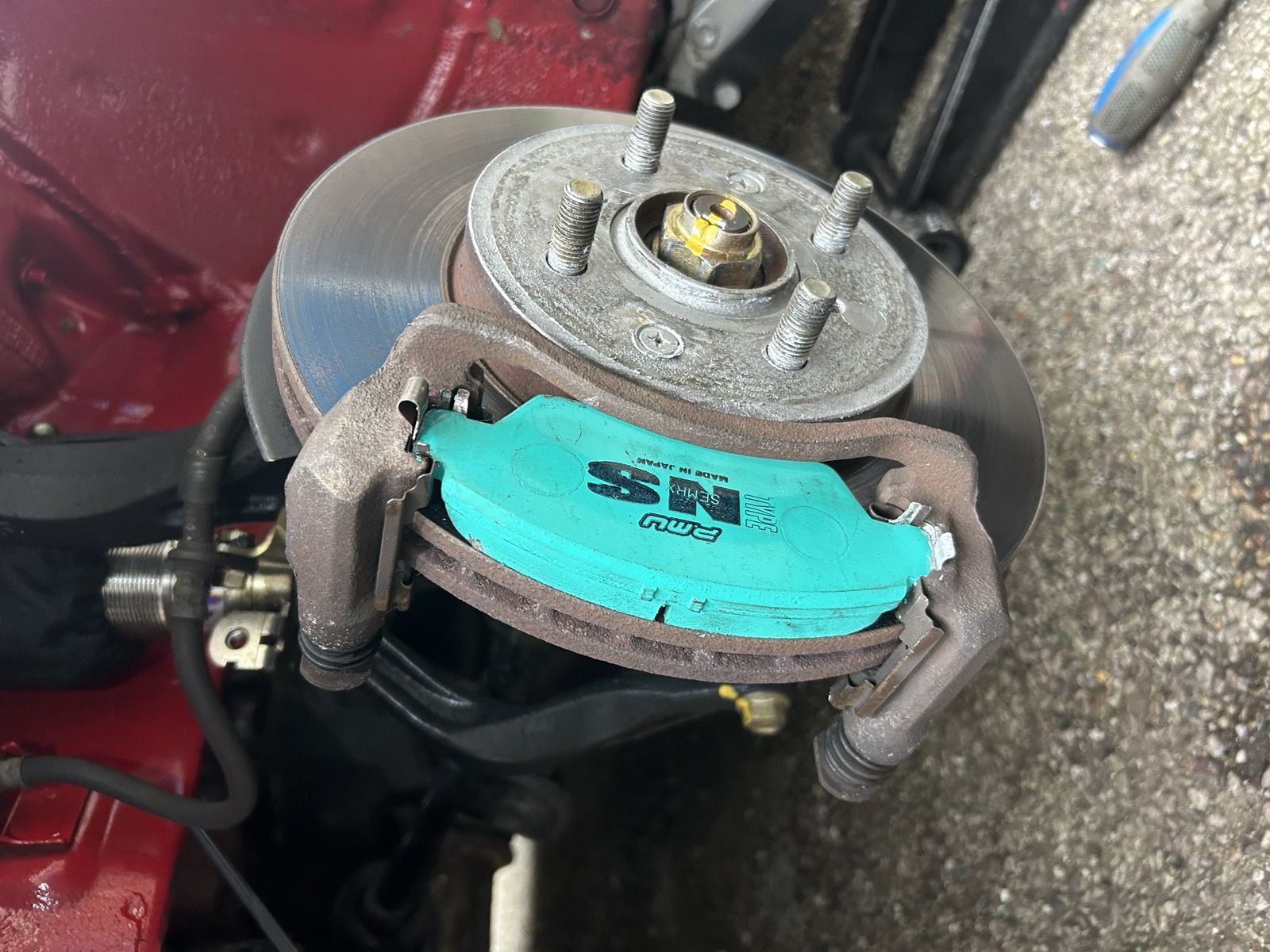 A teal Project Mu brake pad installed in the front caliper, with a new disc, on the red Civic