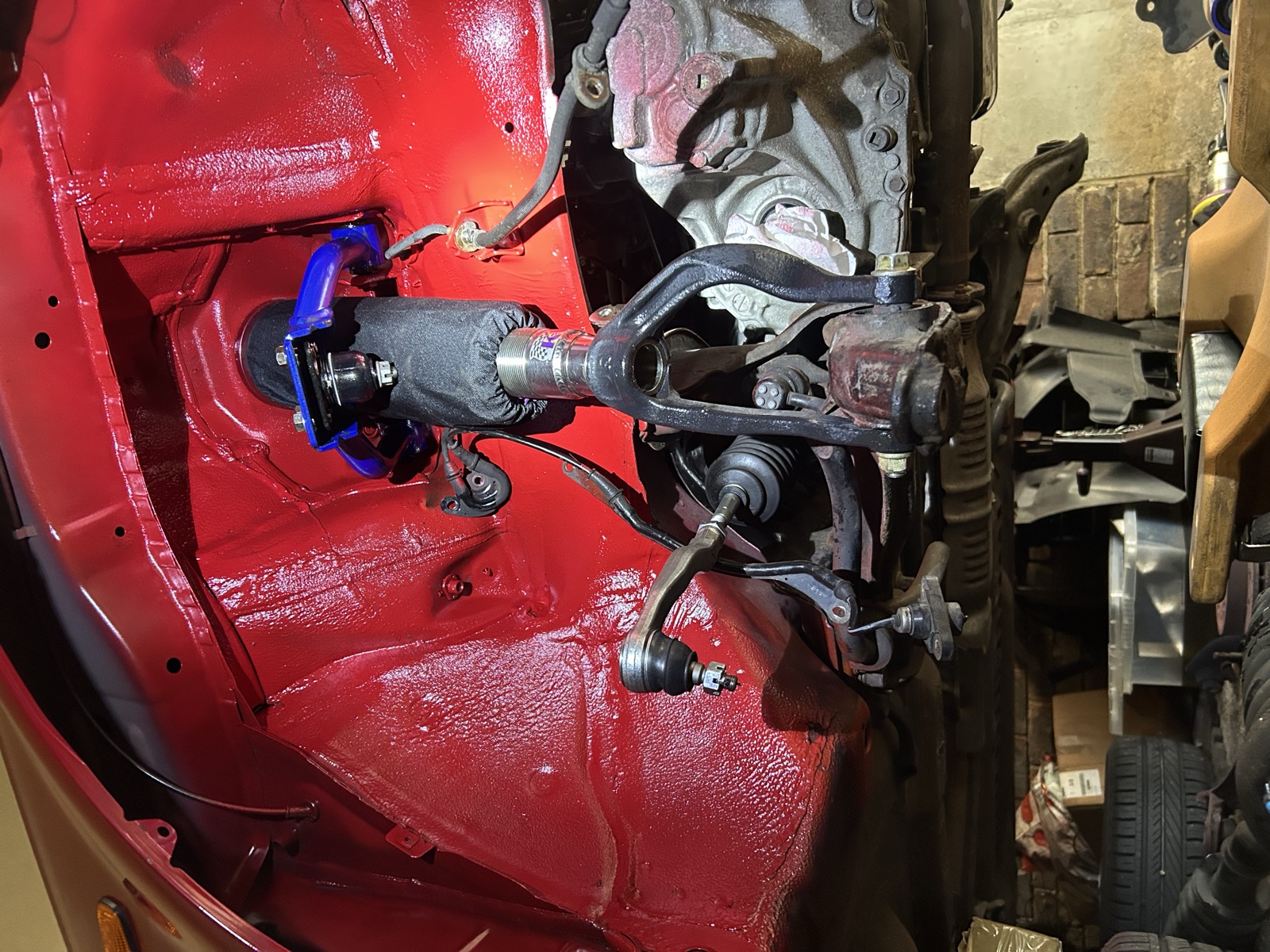 Freshly painted red underside of the car around the front strut mount, with a new coilover top mount installed
