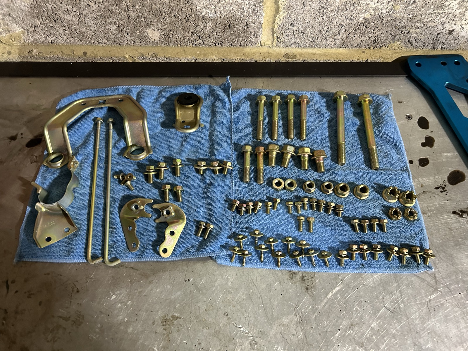 Rows of zinc-plated bolts, nuts, and brackets laid out on a cloth, organized by size